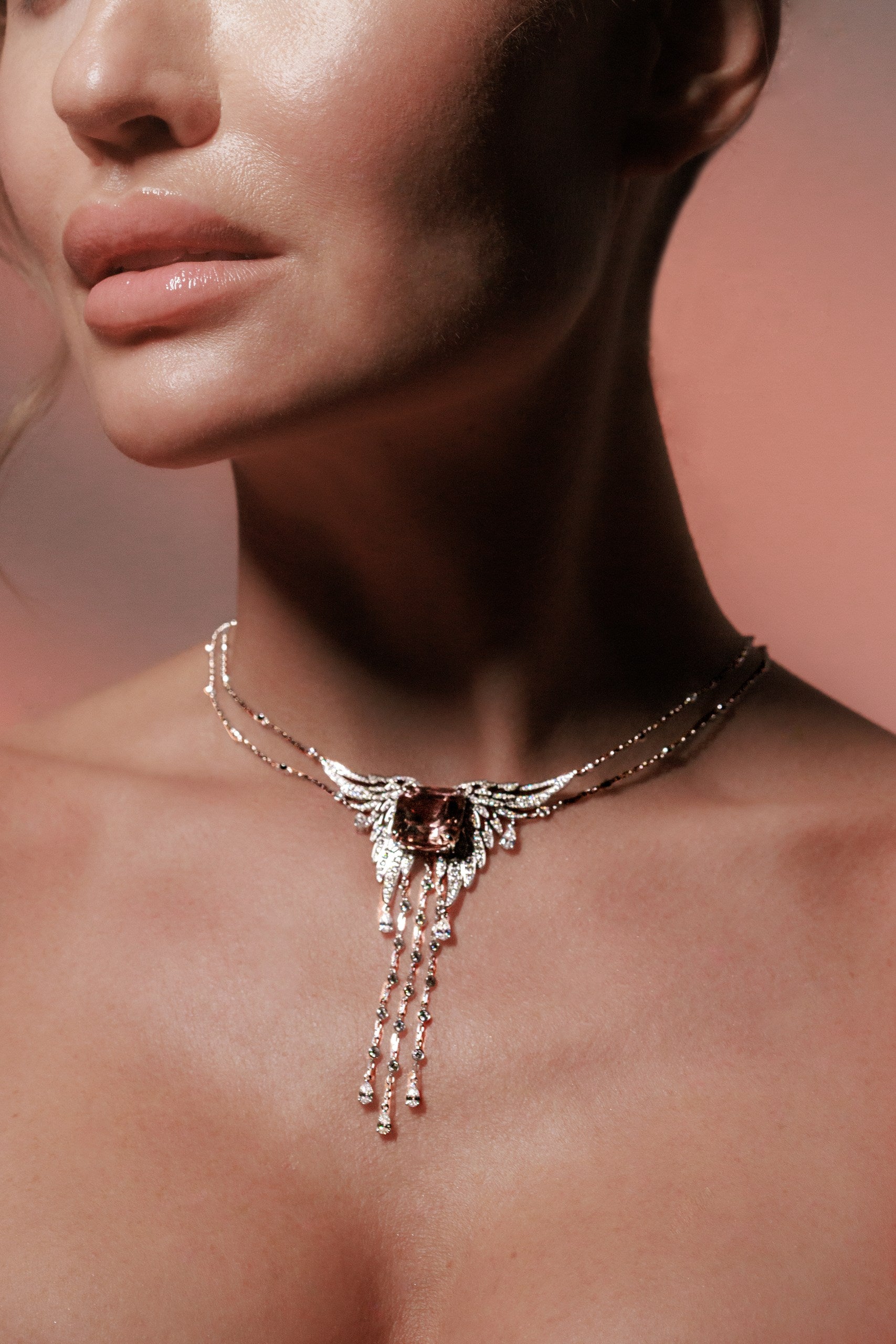 Close-up of a woman wearing an elegant necklace with a pink background